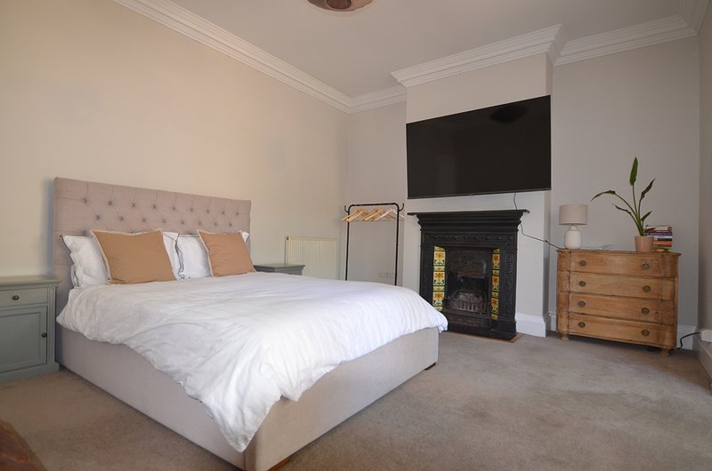 Spacious bedroom with double bed, fireplace, TV, wooden dresser and side table