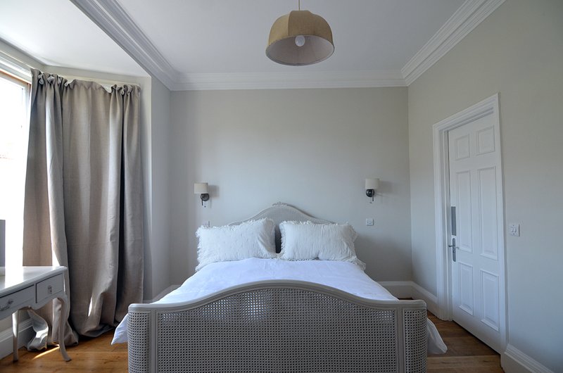 Bright bedroom with white double bed, grey headboard, pendant light, and cream curtains