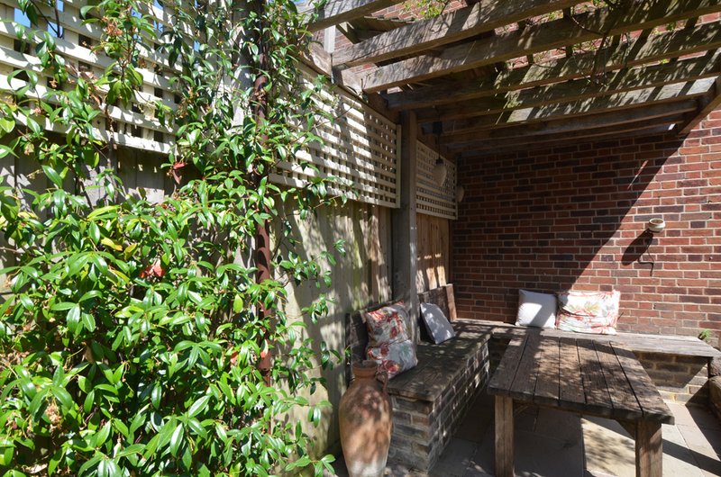 Brick patio with wooden pergola, climbing ivy, and shaded seating area