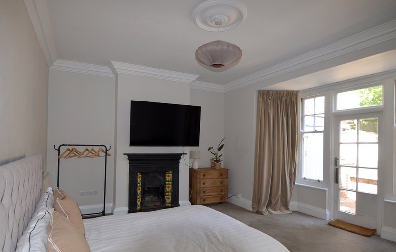 Bright bedroom with double bed, fireplace, TV, wooden dresser and patio doors