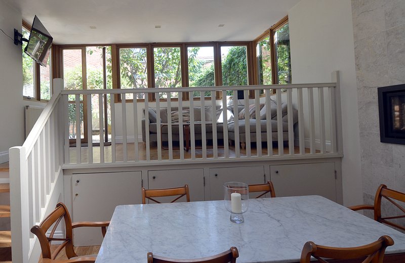 Bright dining area with wooden chairs, white railing, and large multi-pane windows overlooking garden