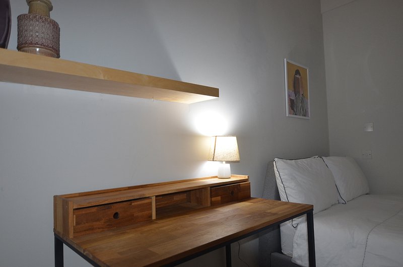 Bedroom with wooden desk, floating shelf, table lamp, and bed with grey bedding