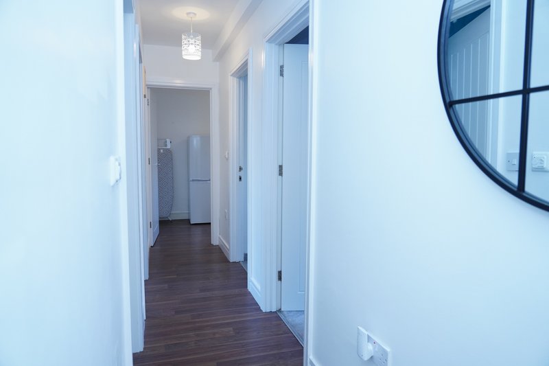 Clean hallway with white walls, dark wood flooring, multiple doors and round mirror