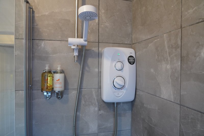 Bathroom shower cubicle with rainfall showerhead, electric water heater, and toiletries dispenser