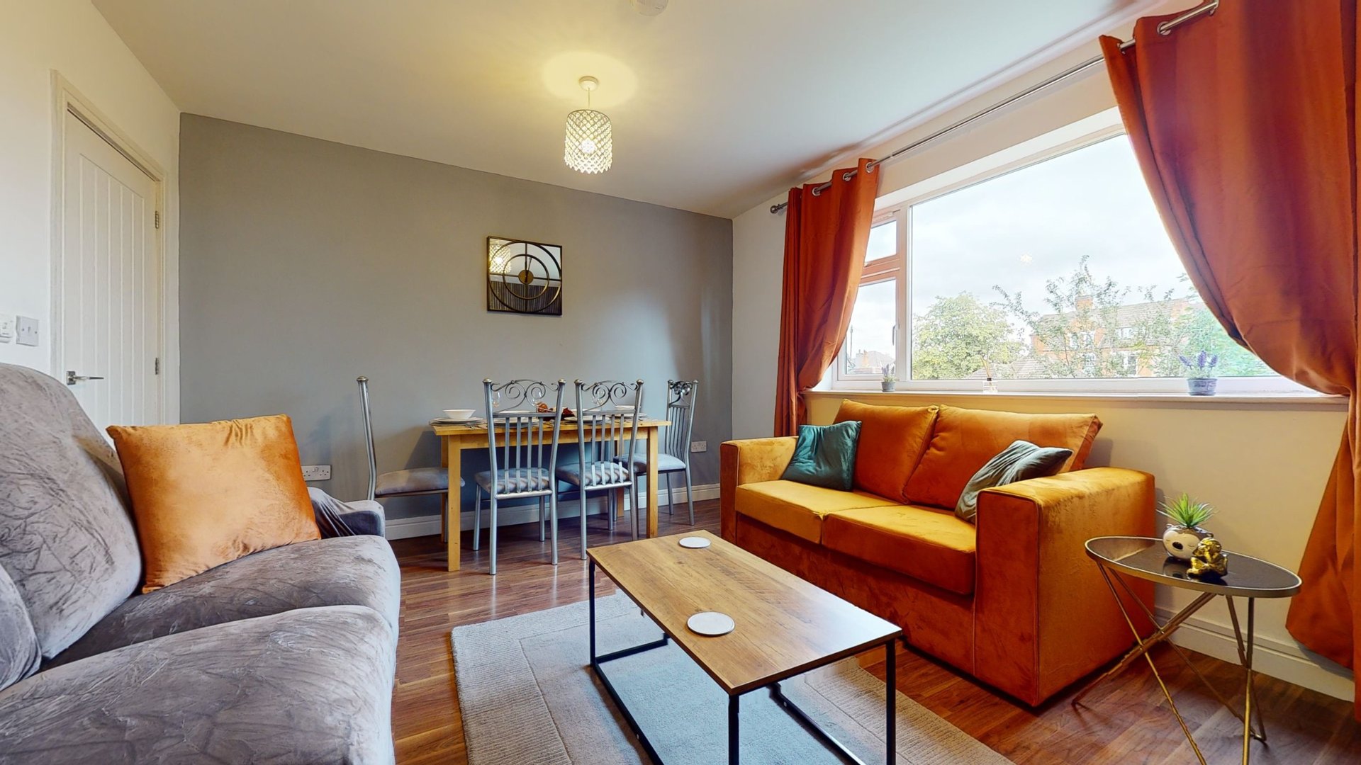 Bright living room with gray sofa, orange armchair, wooden dining table and large windows with red curtains