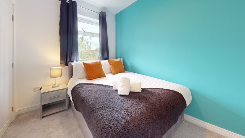 Bright modern bedroom with double bed, turquoise accent wall, and dark curtains