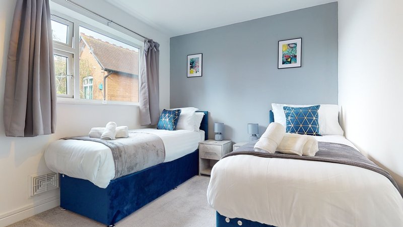 Twin bedroom with blue bed frames, white bedding, decorative cushions and window with curtains