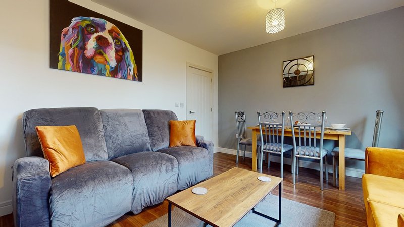 Open-plan living and dining area with grey sofa, wooden coffee table, and dining chairs