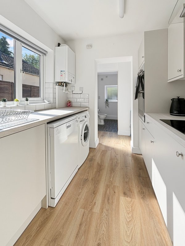 Modern kitchen with white cabinetry, washing machine, wooden flooring and large window
