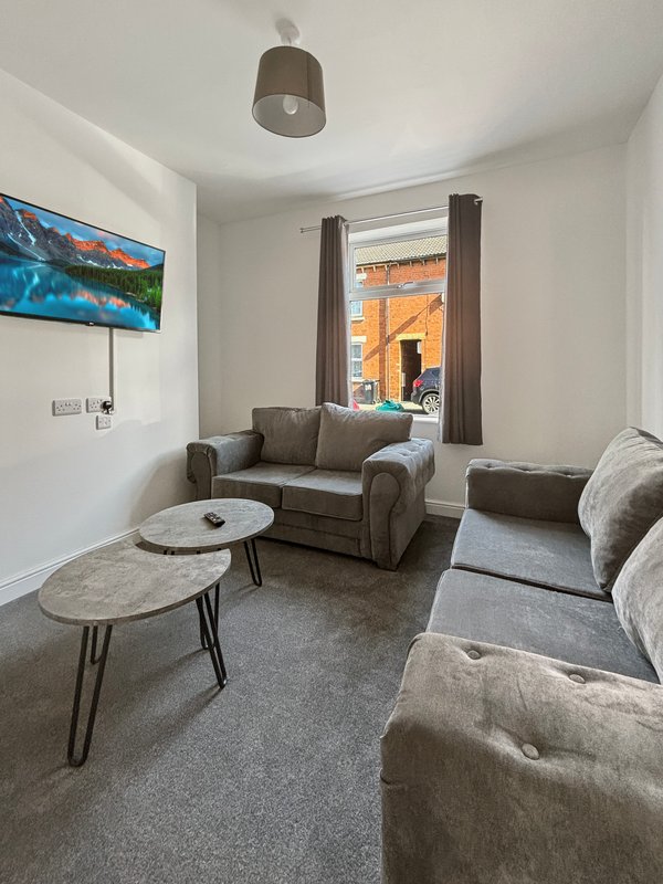Bright living room with grey sofas, coffee tables, wall-mounted TV and large window with orange building visible outside