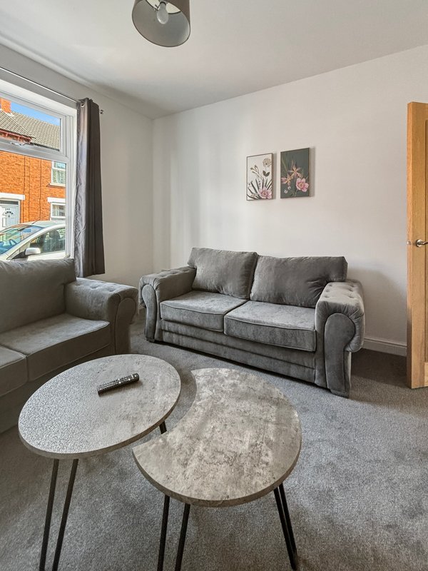Living room with gray sofa, round coffee tables, window with street view, and wall art