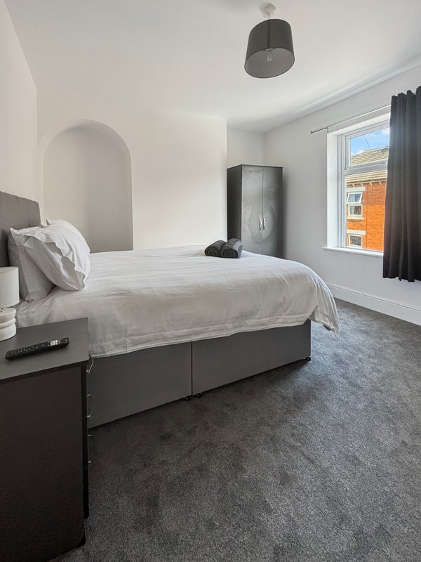 Modern bedroom with double bed, grey headboard, pendant light and window with street view