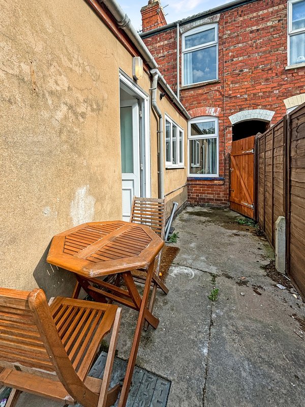 Outdoor side passage with wooden chairs, brick buildings, and wooden gate