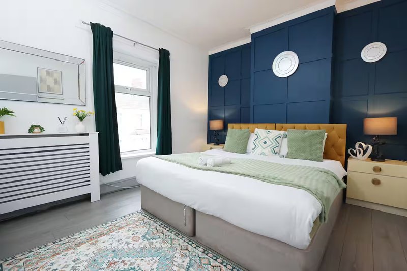 Modern bedroom with double bed, dark blue accent wall, green bedding, and wooden headboard