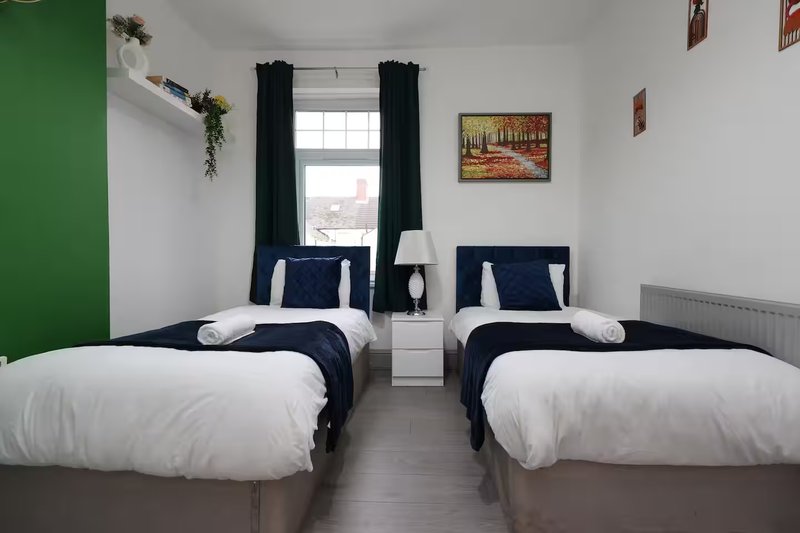 Twin bedroom with two single beds, dark curtains, window and green accent wall