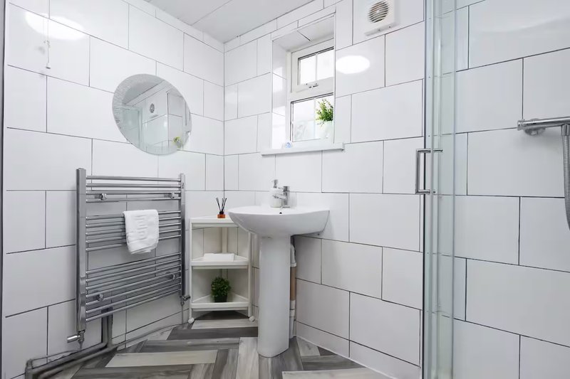 Modern bathroom with white subway tiles, pedestal sink, heated towel rail and shower enclosure