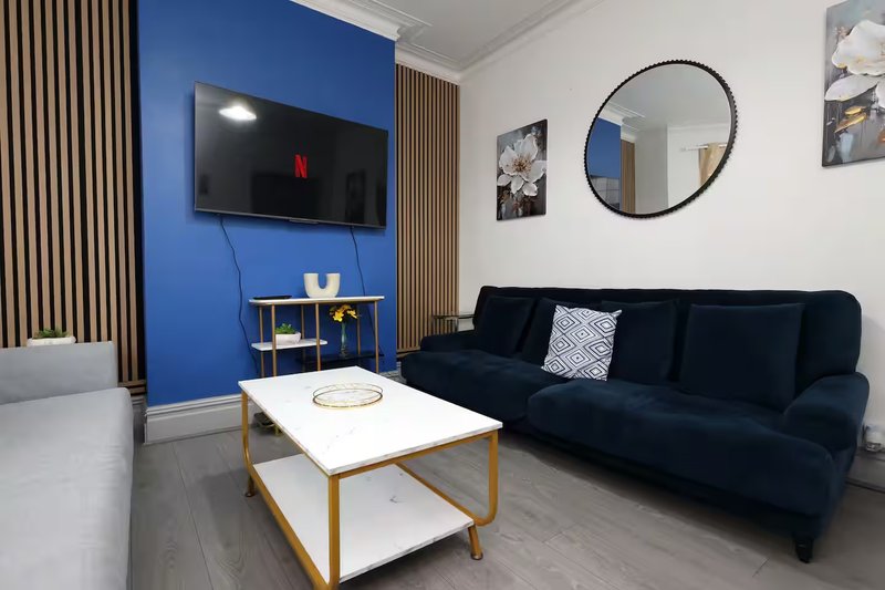 Modern living room with dark blue sofa, wall-mounted TV, round mirror and wooden coffee table