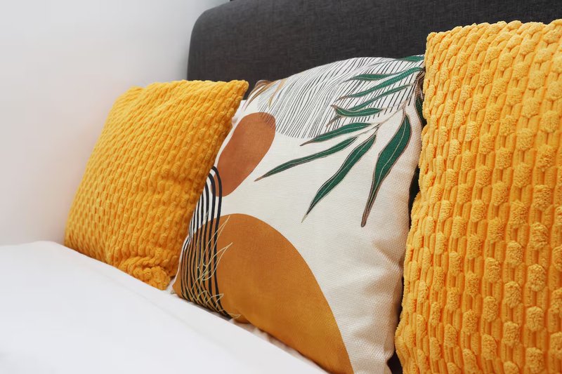 Bed with yellow textured cushions, decorative pillow with botanical print, white bedding and dark headboard