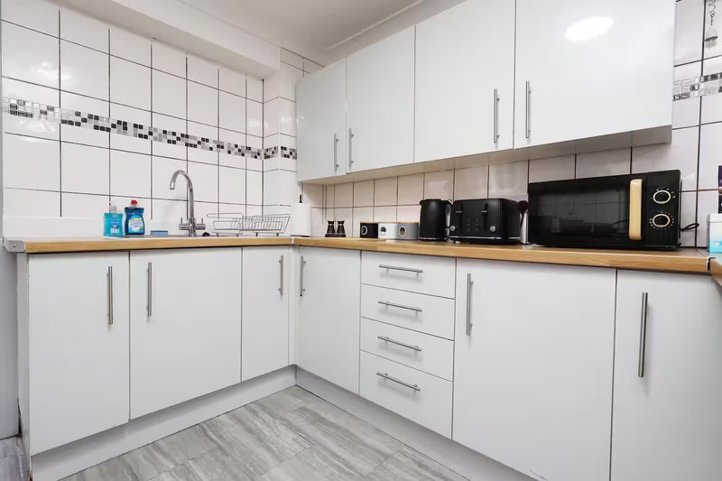 Modern kitchen with white cabinets, wooden countertop, stainless steel sink and black appliances