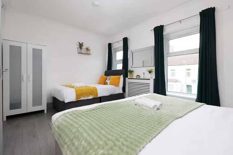 Bright bedroom with two beds, dark curtains, white furniture and wooden flooring