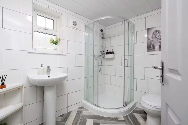 Modern bathroom with white tiles, pedestal sink, shower enclosure, toilet and window