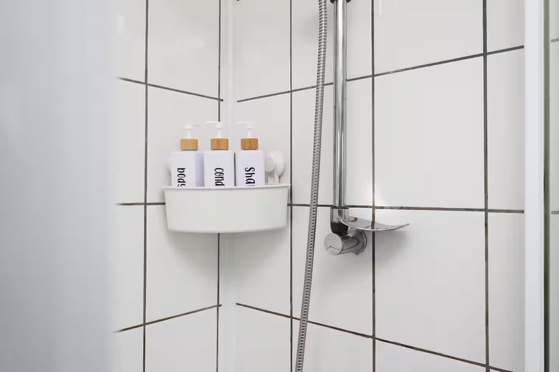 Modern white bathroom wall with tiled grid pattern, shower fixtures, and toiletry bottles on shelf