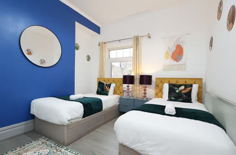 Bright twin bedroom with blue accent wall, two single beds, mustard cushions and decorative wall art