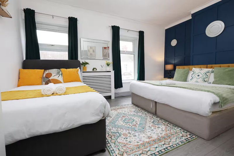 Bright bedroom with two beds, navy accent wall, yellow and green bedding, black curtains