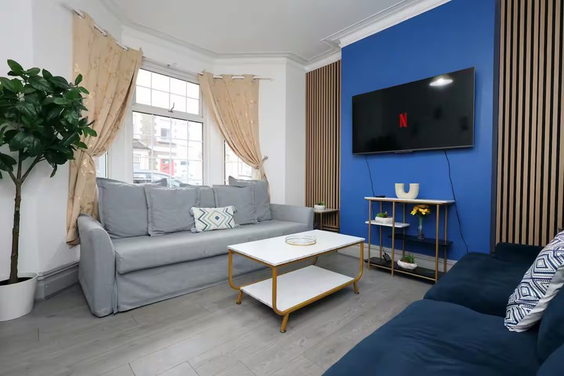 Modern living room with gray sofa, blue accent wall, TV, and wooden coffee table
