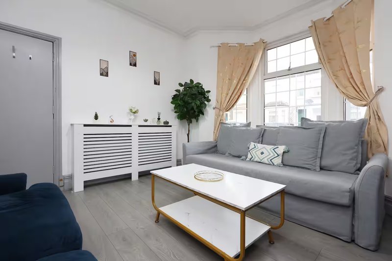 Bright living room with gray sofa, white storage cabinet, coffee table and large windows with curtains