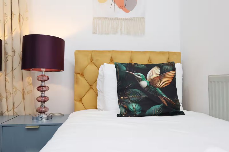 Bedroom with yellow upholstered headboard, white bedding, decorative pillows and table lamp