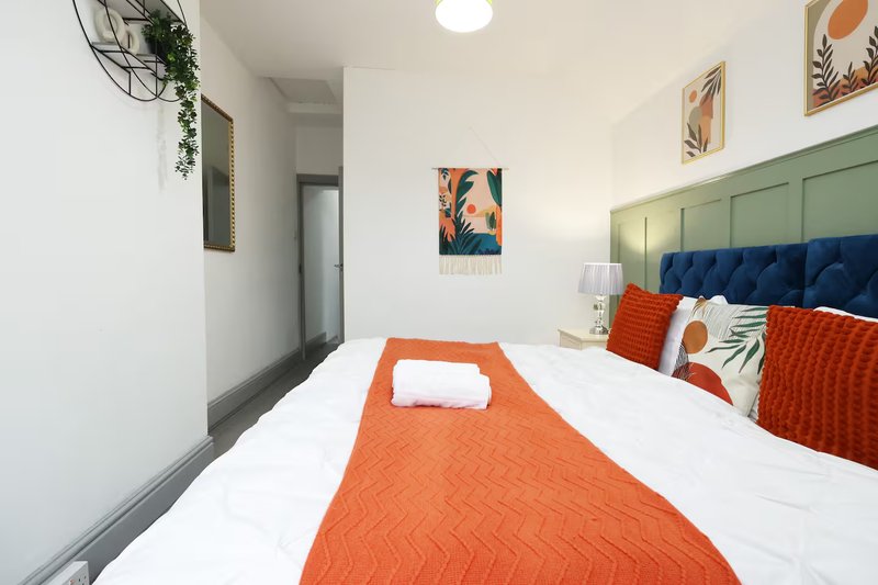 Modern bedroom with blue headboard, orange bedding, white sheets and decorative wall art