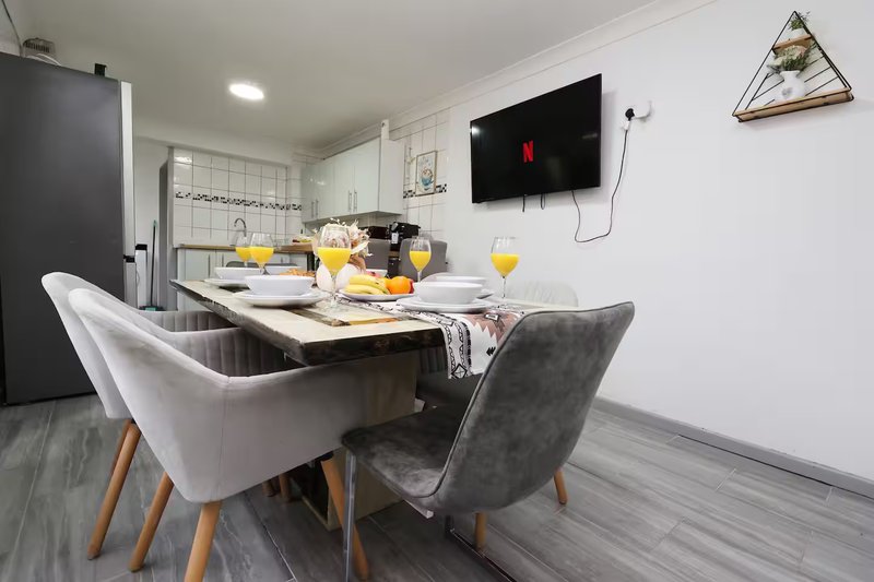 Modern kitchen and dining area with table, chairs, wall-mounted TV and yellow flowers in vases
