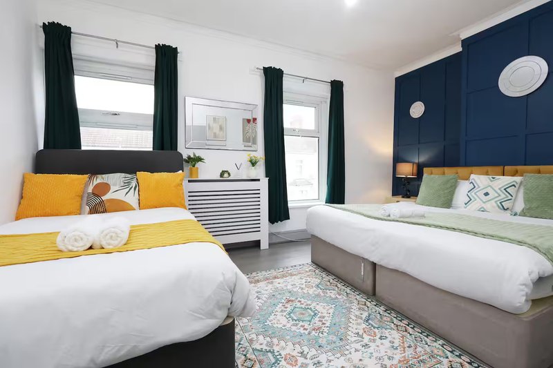 Modern twin bedroom with yellow and green bedding, dark blue feature wall, black curtains and windows
