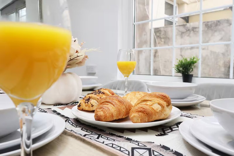 Breakfast table with croissants, orange juice, and place settings by window