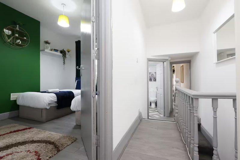 Modern hallway with white walls and grey flooring, leading to bedroom with green accent wall and double bed
