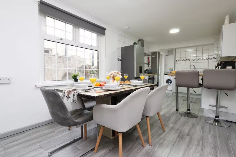 Modern open-plan kitchen and dining area with dining table, upholstered chairs, and large windows