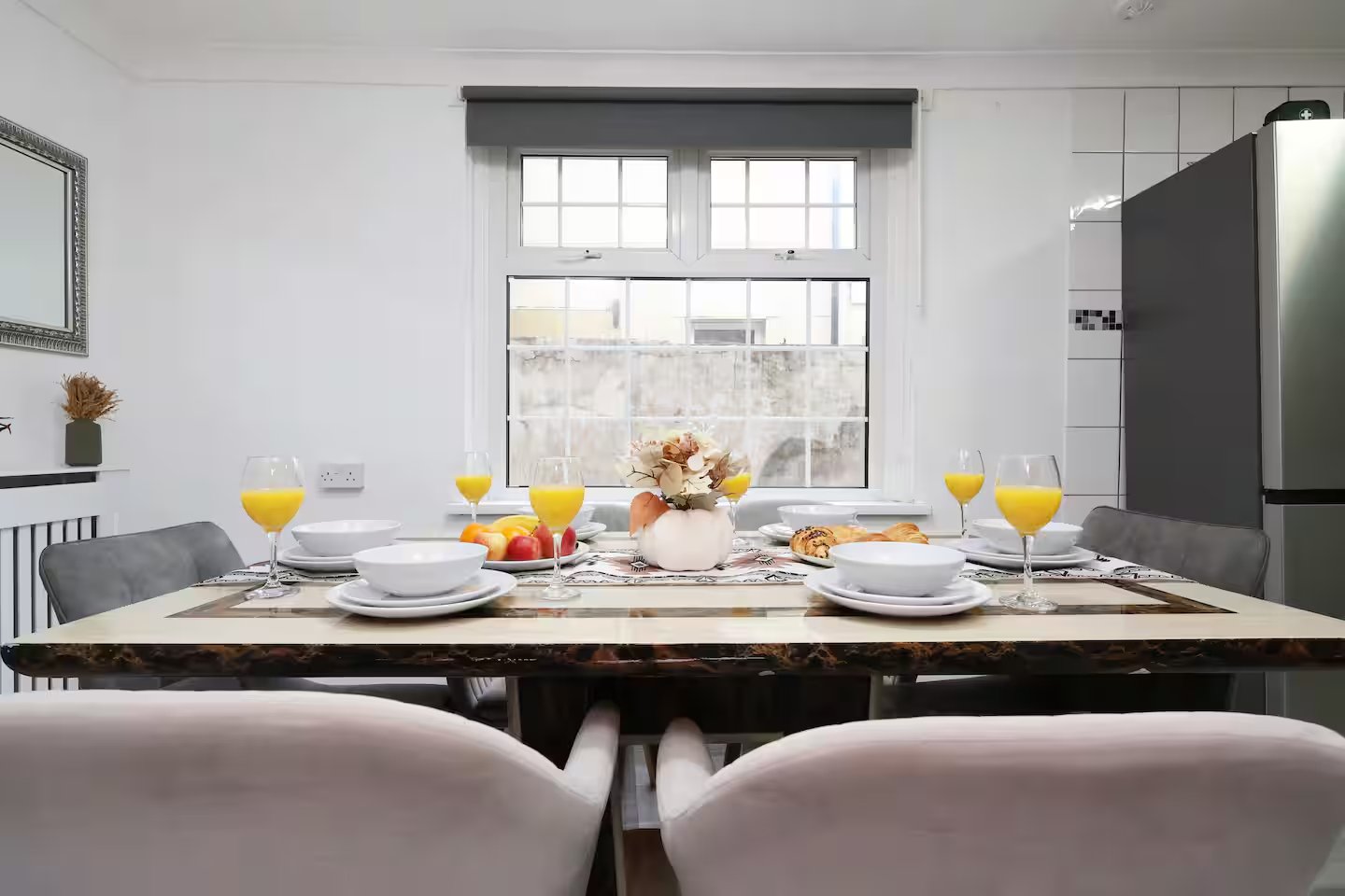 Modern dining room with set table, orange juice glasses, windows overlooking street, and contemporary kitchen
