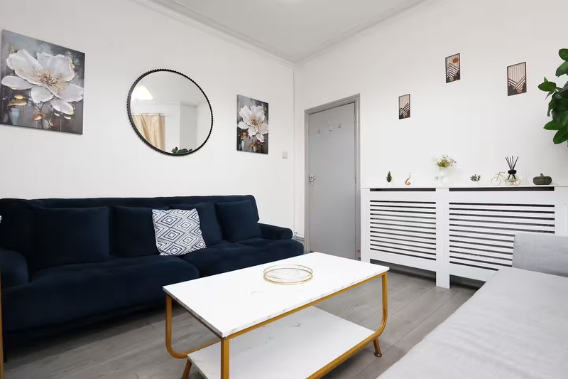 Bright living room with dark blue sofa, round wall mirror, white storage units and wooden coffee table