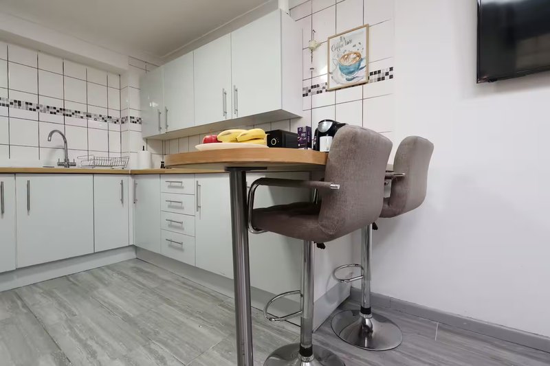 Modern kitchen with white cabinetry, breakfast bar with gray upholstered stools, and wall-mounted TV