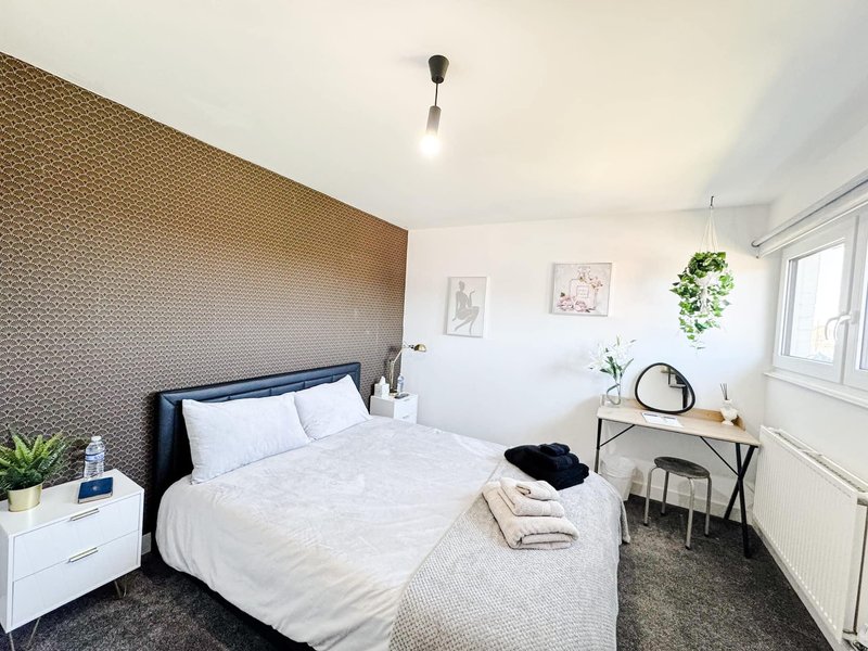 Modern bedroom with double bed, textured accent wall, white bedside table and desk area