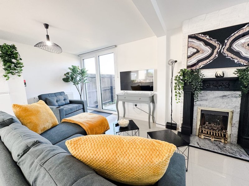 Modern living room with grey sofas, yellow cushions, fireplace, TV, and glass doors to balcony