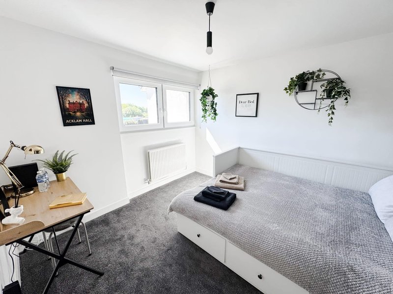 Bright modern bedroom with double bed, desk, potted plants and large window