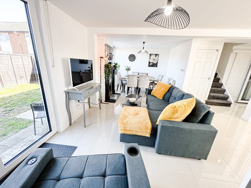 Open-plan living room with grey sofa, yellow cushions, TV stand, and garden view through patio doors