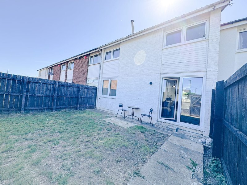 Modern terraced house exterior with patio area, blue fencing, and small garden