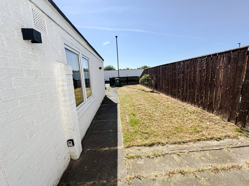 Modern white-brick bungalow exterior with garden, wooden fence and driveway