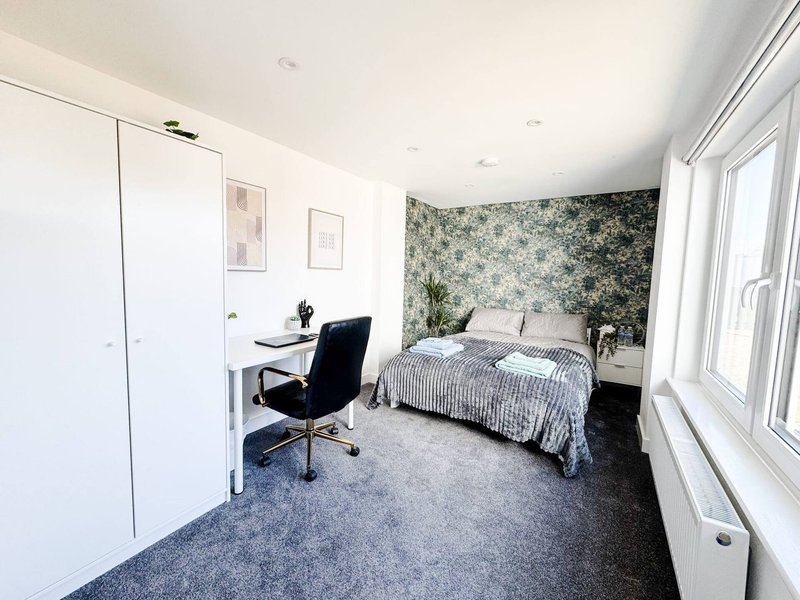 Bright bedroom with double bed, desk, office chair, floral accent wall and large windows