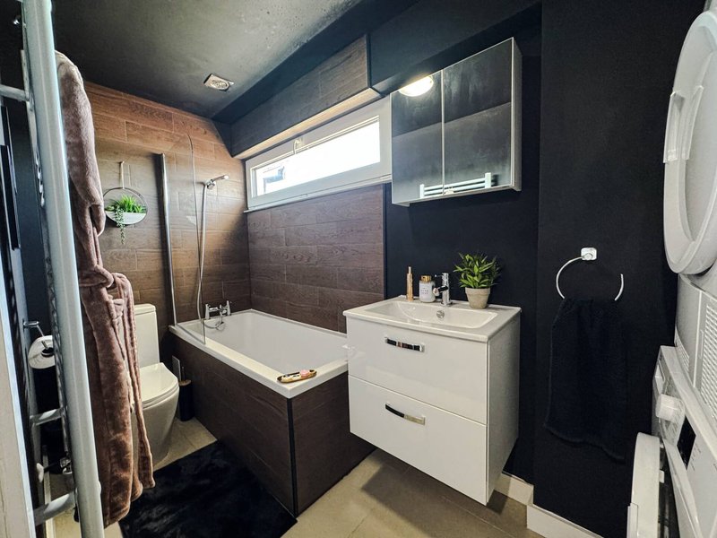 Modern bathroom with brown tile walls, white vanity, bathtub, and dark ceiling