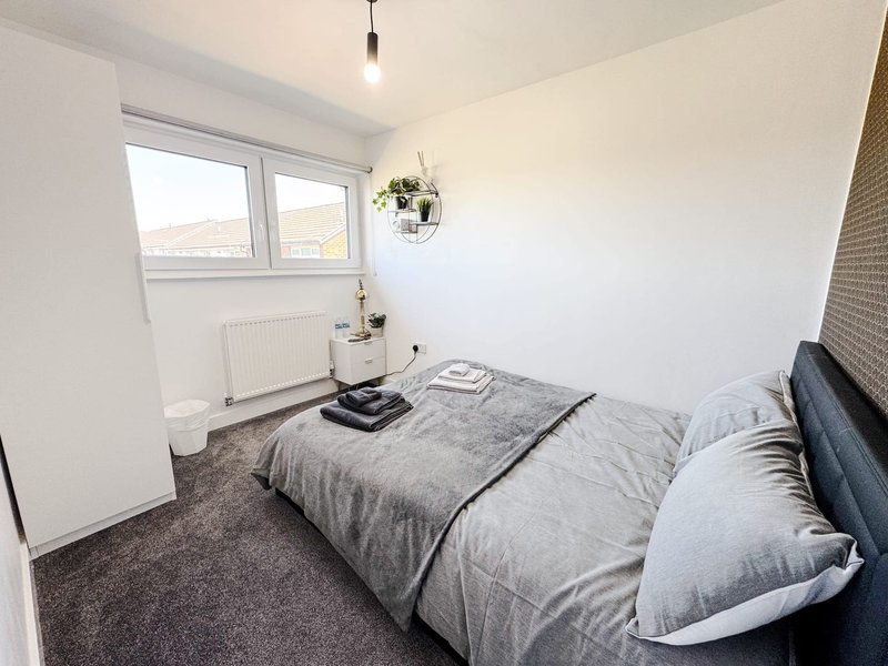 Bright modern bedroom with double bed, dark headboard, window with radiator and pendant light