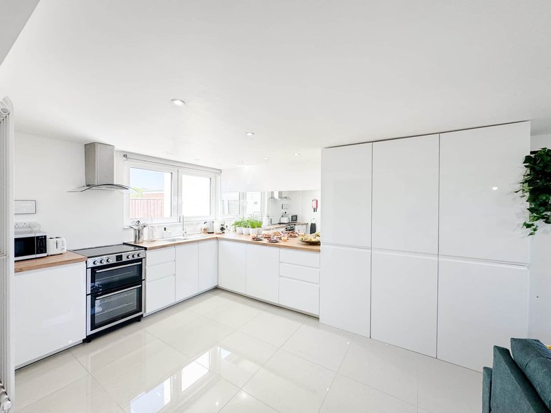 Modern white kitchen with double oven, stainless steel hood, and light tiled flooring